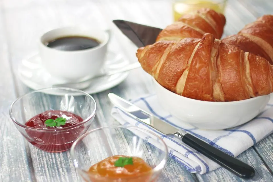 A croissant with coffee, jam and butter on a table