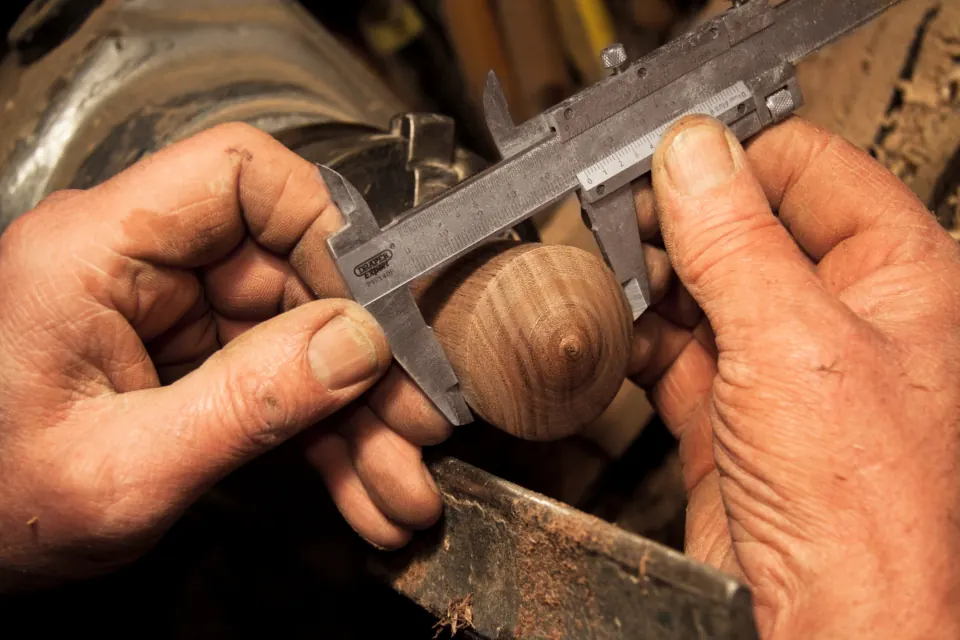 Hands measuring a turned wooden knob with calipers